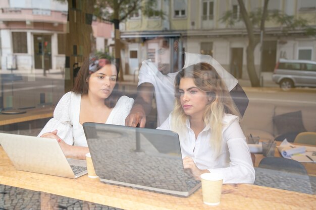 Multiethnische Designer diskutieren Projekt drinnen hinter dem Fenster