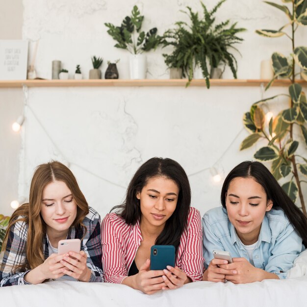 Multiethnische Freunde, die an den Telefonen auf Bett schreiben