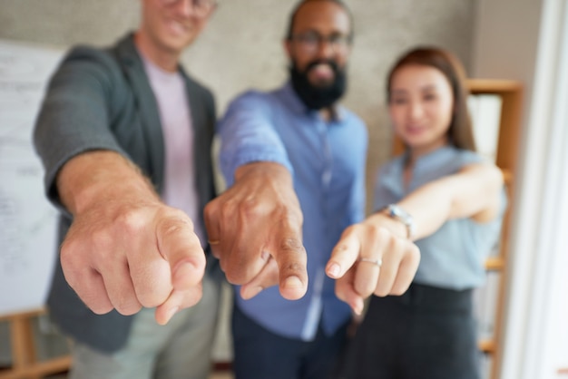 Multiethnische Kollegen, die im Büro mit den ausgestreckten Armen stehen und auf Stelle zeigen