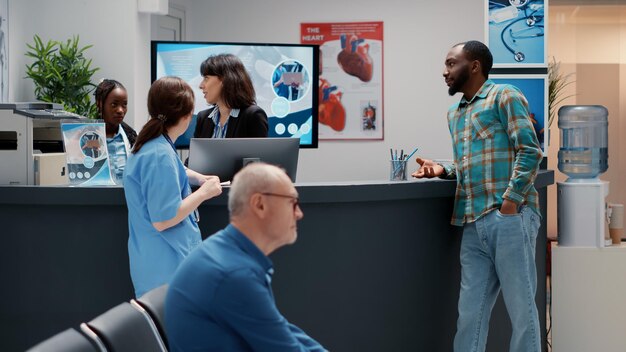 Multiethnische Menschen unterhalten sich über die Unterstützung des medizinischen Systems, afroamerikanische Patienten und Krankenhausangestellte sprechen über Kontrolltermine. Wartebereich-Lobby in einer Gesundheitseinrichtung.