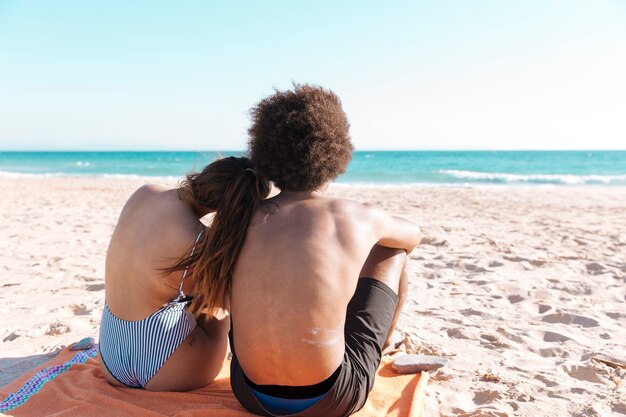 Multiethnische Paare, die auf Strand sitzen