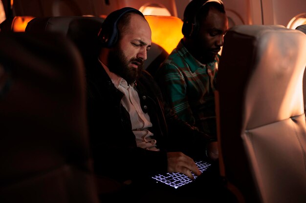 Multiethnische Touristen, die im Flugzeug auf einem kommerziellen Flug sitzen, um auf Arbeitsreise oder Urlaub mit internationalem Luftverkehrsdienst zu reisen. Passagiere, die in der Economy-Klasse für den Transport fliegen.