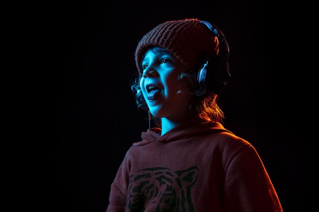Musik hören und tanzen. Porträt des kaukasischen Jungen auf dunklem Studiohintergrund im Neonlicht. Schönes lockiges Modell.