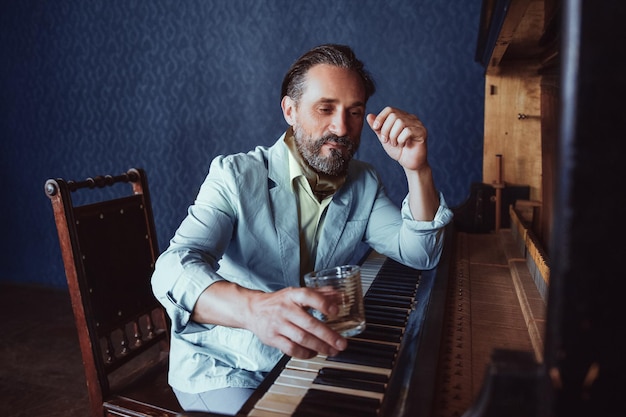 Musiker am Klavier komponiert Musik. In seiner Hand ein Glas alkoholisches Getränk