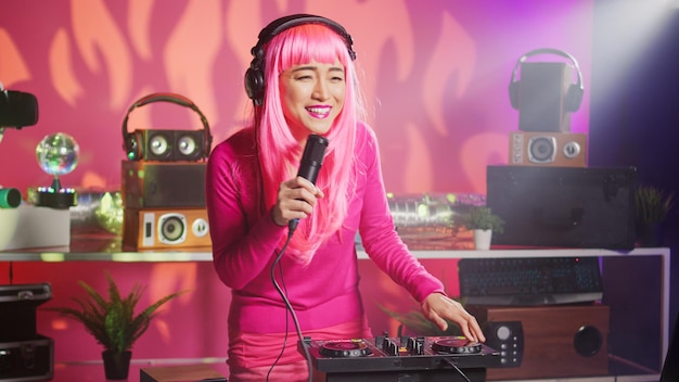 Musiker, der Spaß daran hat, Techno-Musik auf einer Party im Nachtclub zu spielen, mit professioneller Audioausrüstung. Asiatischer Performer mit rosa Haaren, der elektronischen Sound mit Mischpult mischt. DJ-Konzept