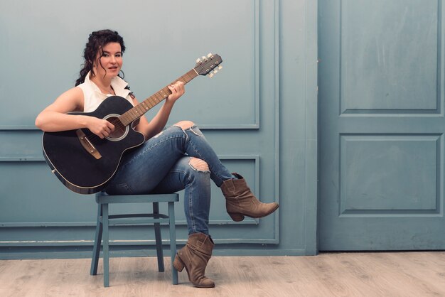 Musiker mit der Gitarre, die auf Stuhl sitzt