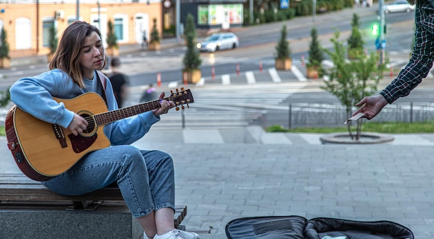 Musikerin als Straßenmusikant spielt Akustikgitarre und singt draußen auf der Straße