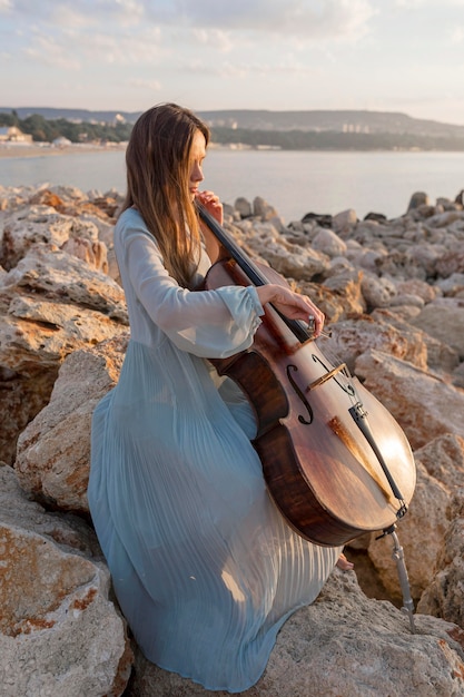 Musikerin, die Cello bei Sonnenuntergang auf Felsen spielt