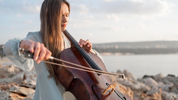 Musikerin, die Cello bei Sonnenuntergang mit Kopienraum spielt