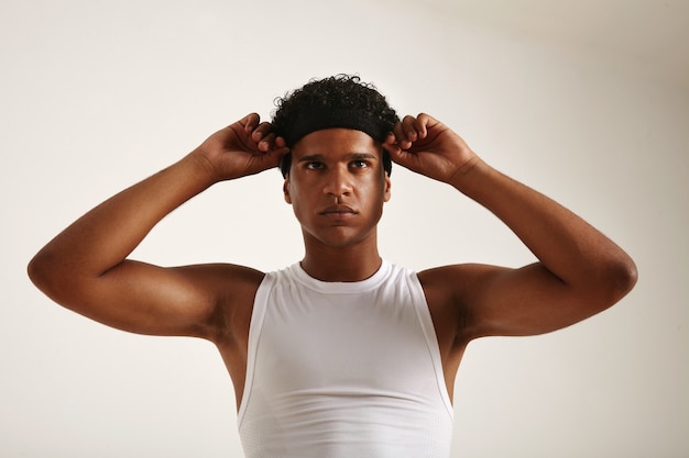 Muskulöser afroamerikanischer Athlet im weißen Basketballhemd, der sein schwarzes Stirnband anpasst und leicht schaut