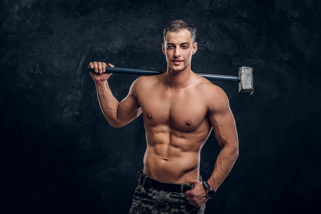 Muskulöser attraktiver heißer Mann hält langen Hammer in der Hand, während er für Fotografen posiert.