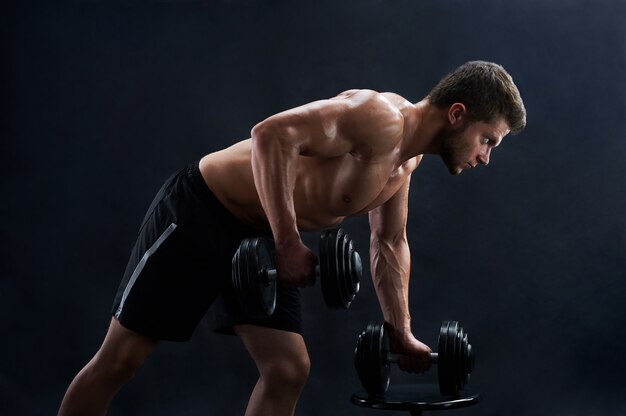 Muskulöser junger Mann, der Gewichte auf schwarzem Hintergrund anhebt