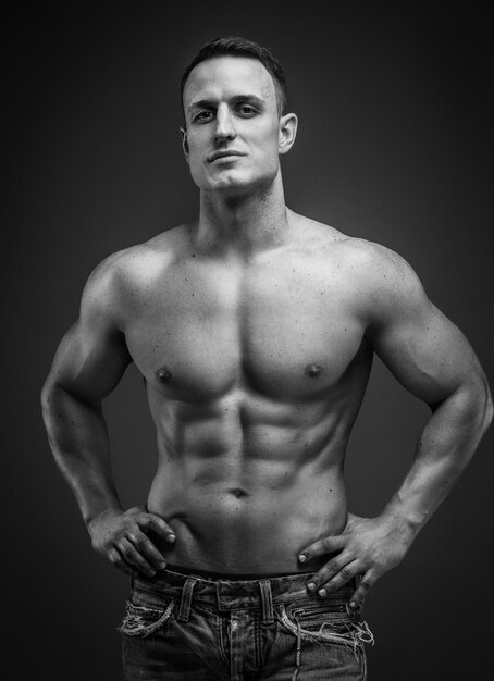 Muskulöser Mann auf grauem Hintergrund zeigt seinen Oberkörper.