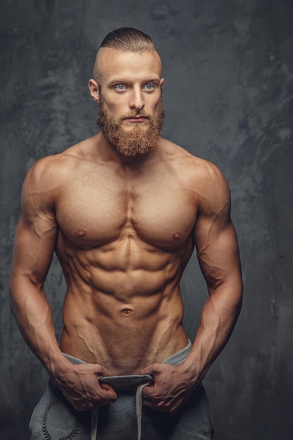 Muskulöser Mann mit Bart, der seinen tollen Körper auf grauem Hintergrund zeigt.