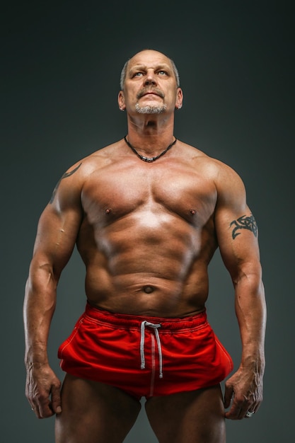 Muskulöser Mann mittleren Alters posiert im Studio. Isoliert auf grau