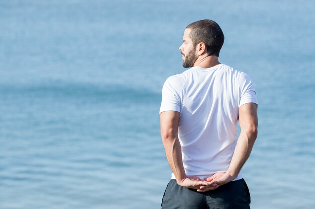 Muskulöser Mann Stretching Arme hinter dem Rücken in See