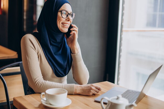 Muslimische Geschäftsfrau, die in einem Café am Computer arbeitet