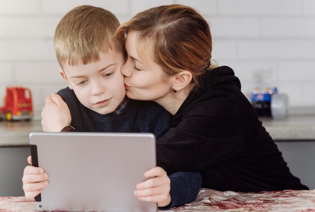 Mutter benutzt Laptop und Tablet und unterrichtet mit ihrem Sohn online zu Hause in seinem Zimmer