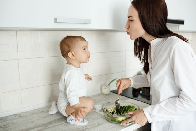 Mutter bereiten Essen vor, während Baby auf Theke sitzt