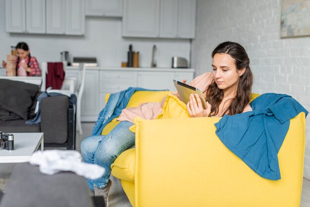 Mutter, die eine Tablette und unscharfe Tochter im Hintergrund verwendet