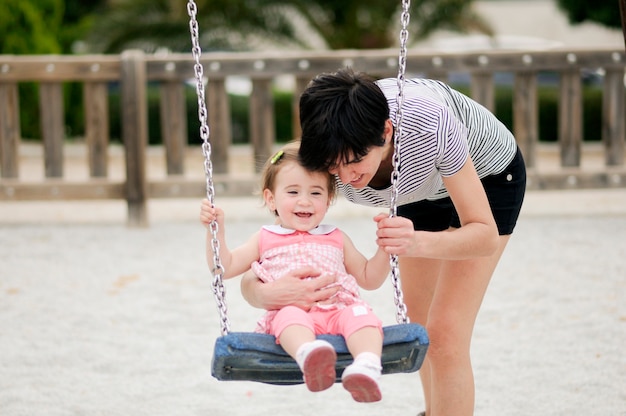 Mutter, die ihre kleine Tochter auf einem Schwingen in einem Spielplatz schwingt