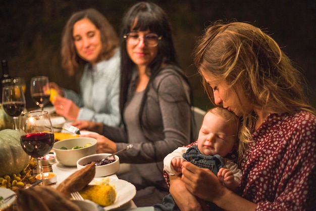 Mutter, die kleines Baby am Familienabendessen küsst