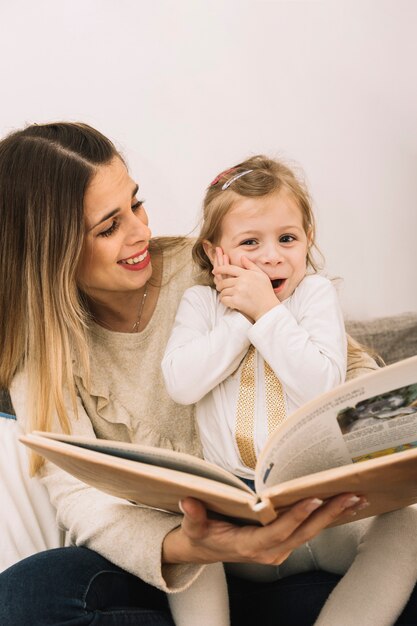 Mutter, die lustiges Mädchen beim Lesen betrachtet