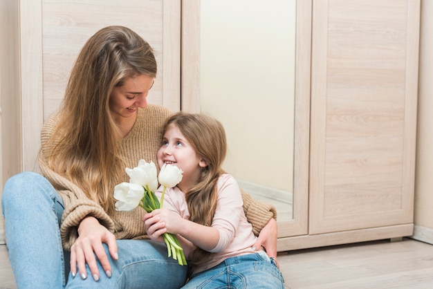 Mutter, die Tochter mit weißen Tulpenblumen umarmt