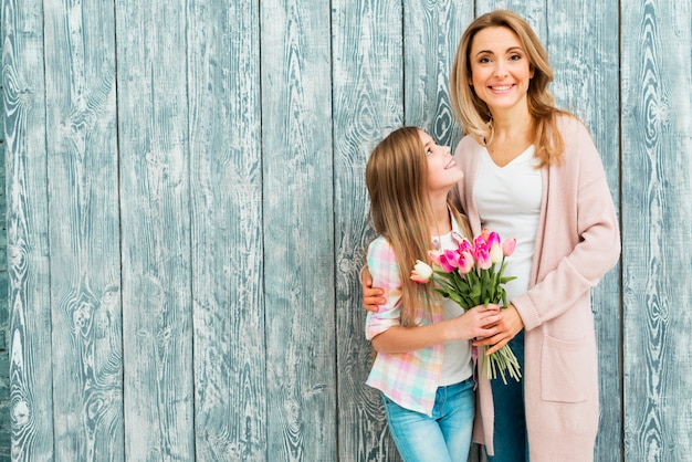 Mutter, die Tochter umarmt und mit Blumen lächelt