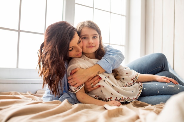 Mutter, die Tochter von hinten auf Bett umarmt