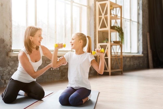 Mutter hilft Tochter, die Gewichte auf Yogamatte hält