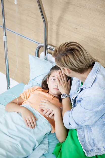 Mutter kümmert sich um ihre Tochter im Krankenzimmer. Sie küsst sie auf die Stirn