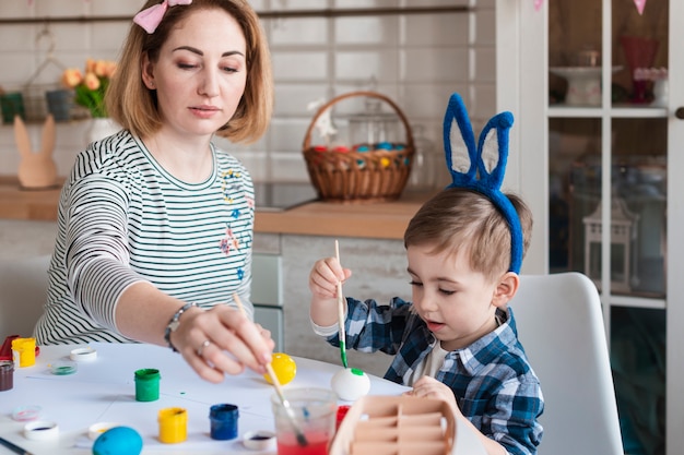 Mutter lehrt kleinen Jungen, wie man Eier für Ostern malt