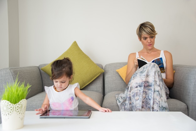 Mutter liest Buch, Tochter spielt mit Tablette