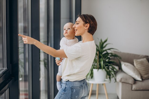 Mutter mit Babysohn steht zu Hause am Fenster