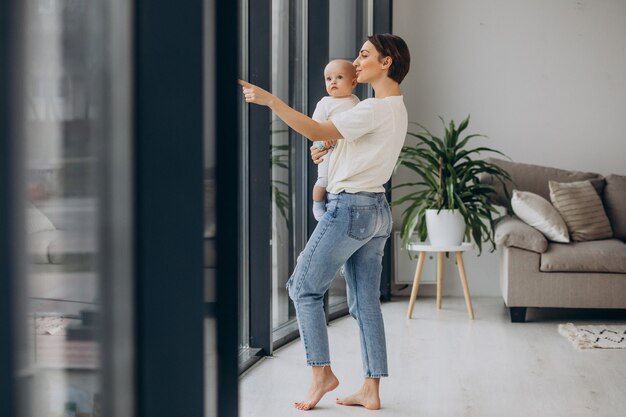 Mutter mit Babysohn steht zu Hause am Fenster