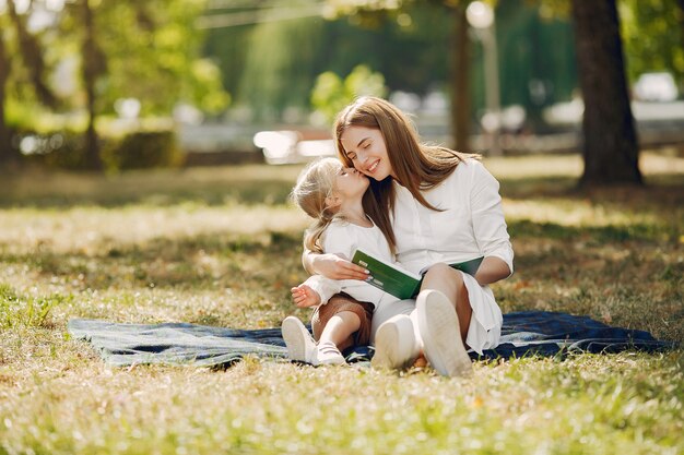 Mutter mit der kleinen Tochter, die auf einem Plaid sitzt und das Buch liest