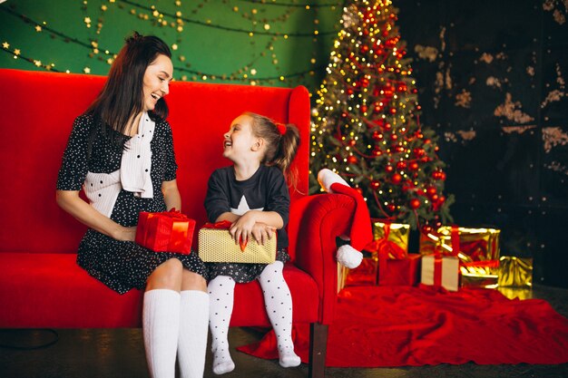 Mutter mit der Tochter auf dem Weihnachten, das auf Sofa mit Geschenken sitzt