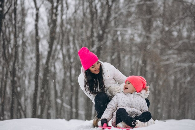 Mutter mit der Tochter, die auf Platte im Winterpark fährt