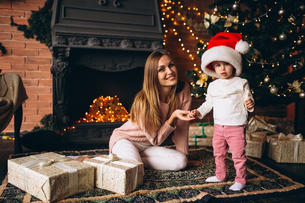 Mutter mit der Tochter, die durch Weihnachtsbaum sitzt