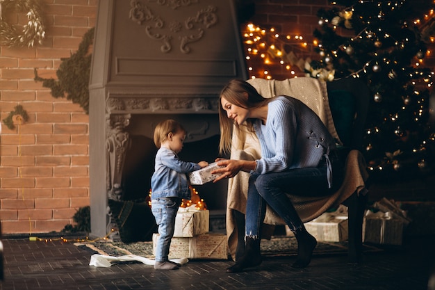 Mutter mit der Tochter, die im Stuhl durch Weihnachtsbaum sitzt