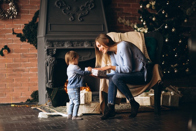 Mutter mit der Tochter, die im Stuhl durch Weihnachtsbaum sitzt