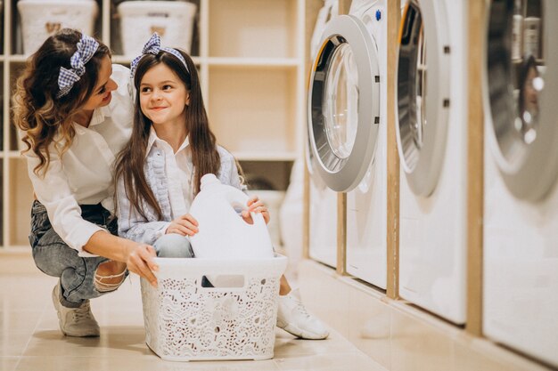 Mutter mit der Tochter, die Wäscherei am Waschsalon der Selbstbedienung tut