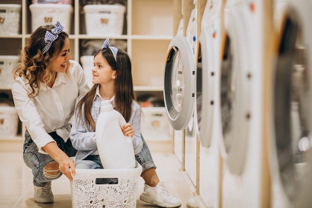 Mutter mit der Tochter, die Wäscherei am Waschsalon der Selbstbedienung tut