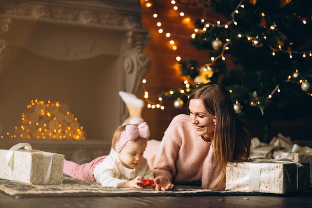 Mutter mit der Tochter, die Weihnachtsgeschenke durch Weihnachtsbaum auspackt