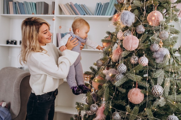 Mutter mit hängenden Spielwaren der kleinen Tochter am Weihnachtsbaum