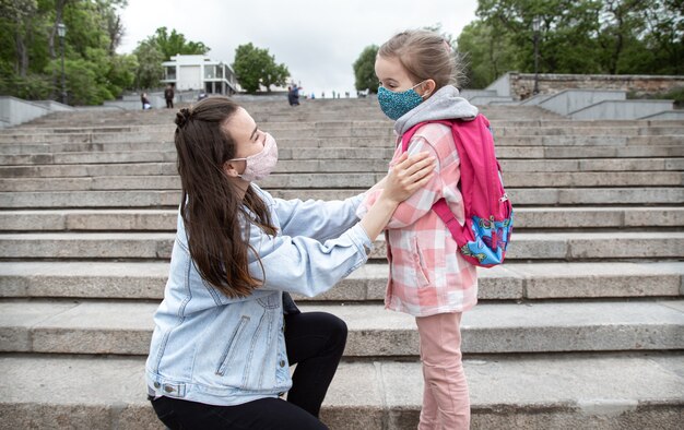 Mutter mit ihrer kleinen Tochter, einem Schulmädchen, auf Stufen auf dem Weg zur Schule. Coronavirus-Pandemie-Bildungskonzept.