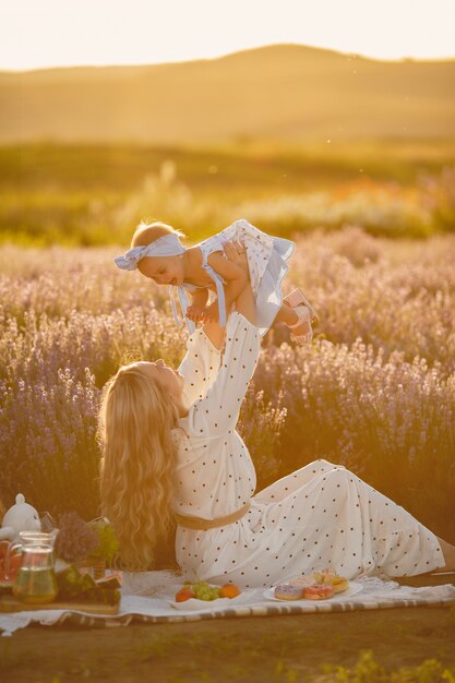 Mutter mit kleiner Tochter auf Lavendelfeld. Schöne Frau und niedliches Baby, das im Wiesenfeld spielt. Familienurlaub im Sommertag.