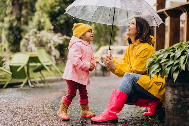 Mutter mit Tochter, die im Regen im Park geht und Gummistiefel trägt