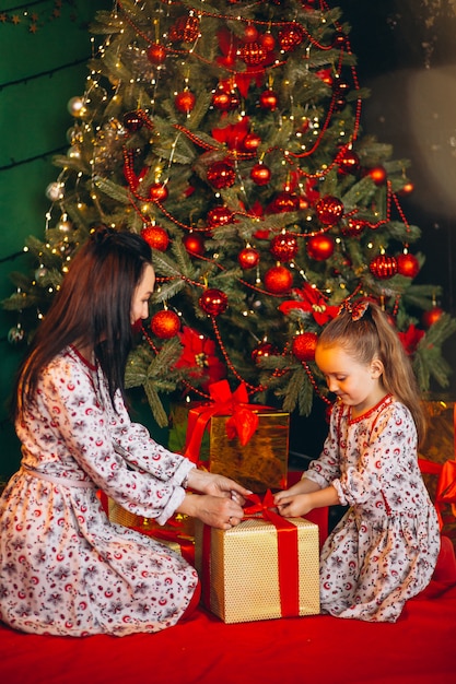 Mutter mit Tochter durch den Weihnachtsbaum, der Geschenke auspackt